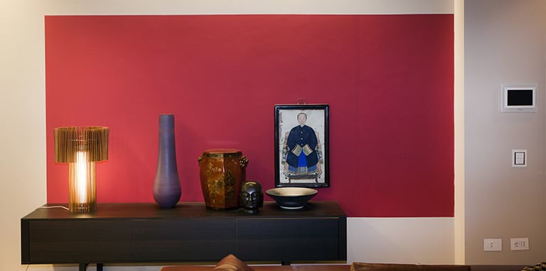 Stol sa svjetiljkom i vazama naspram crveno obojenog zida. Na zidu je obješena slika.