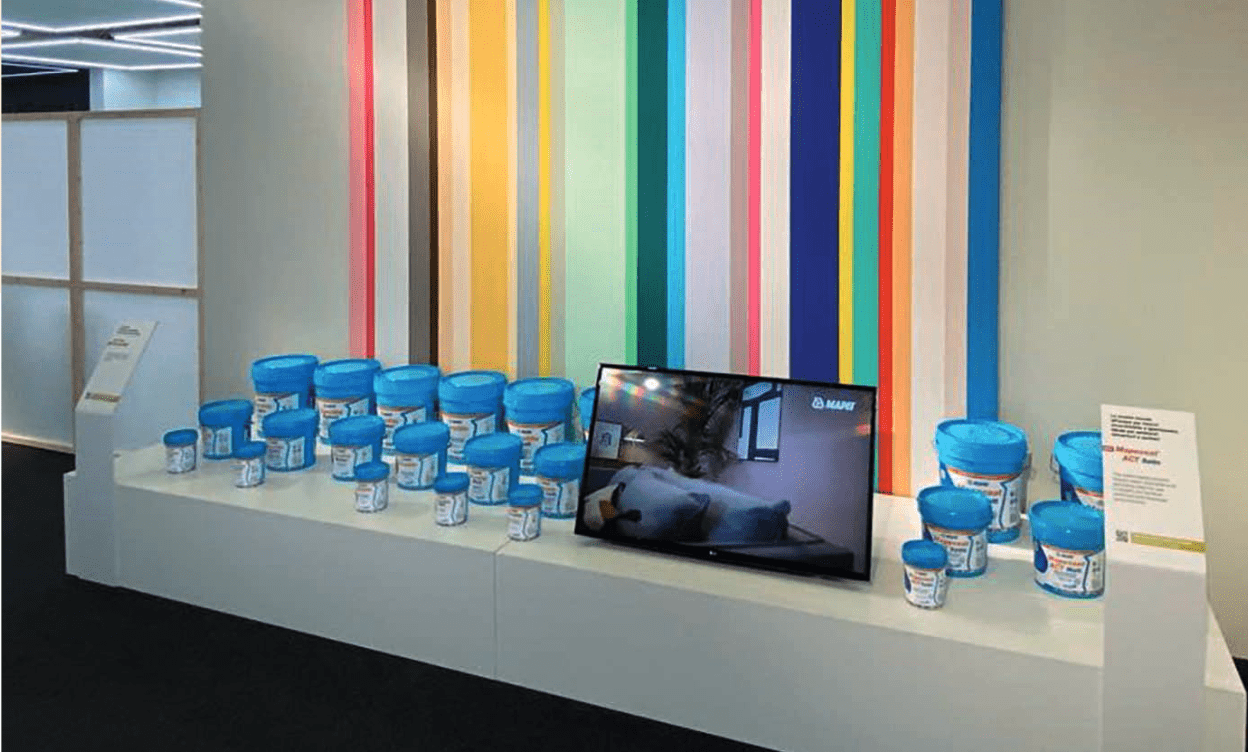 Nekoliko plavih Mapei kutija s bojom i televizor na stolu. Zid je obojan raznobojnim crtama.