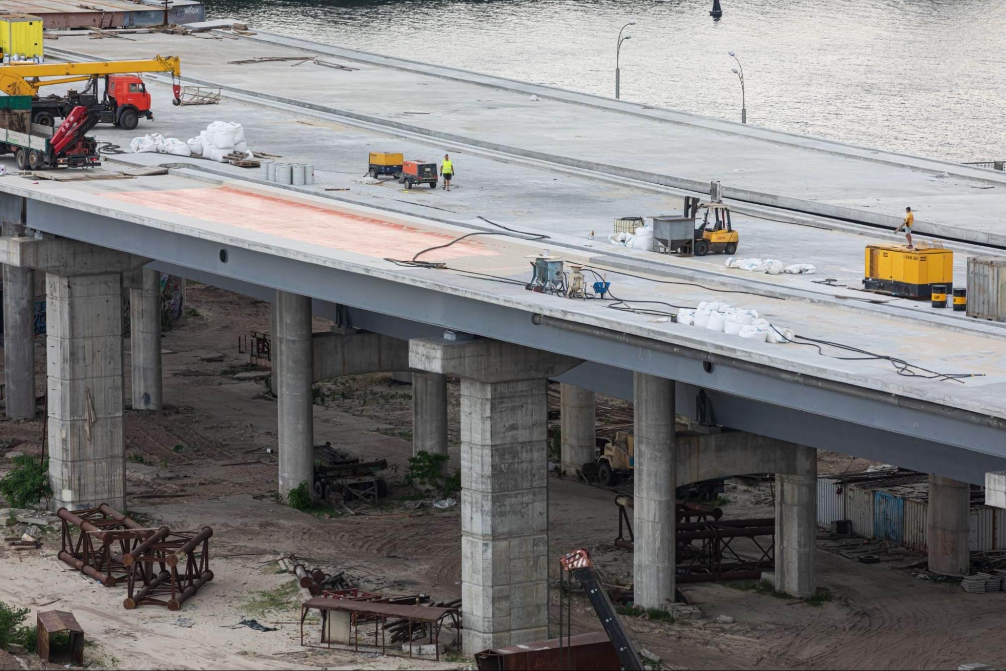 Izgradnja mosta u tijeku. Na mostu su radnici, vozila i pribor za gradnju.