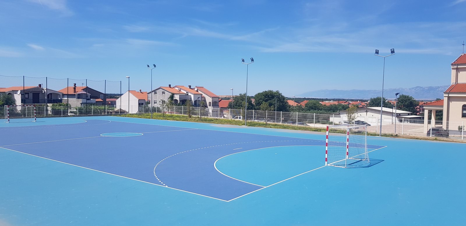 Plavi vanjski sportski teren okružen kućama.