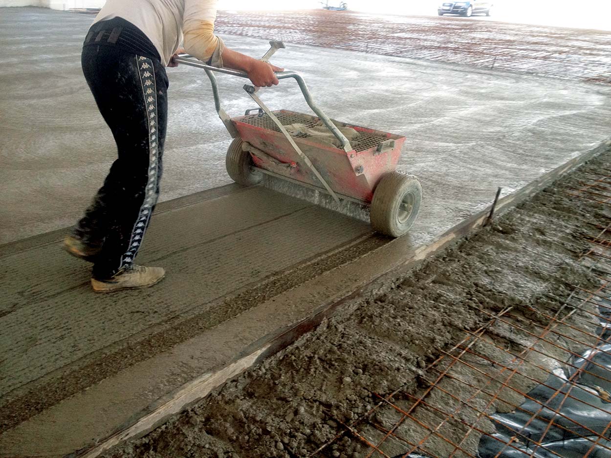 Distribution of the dry-shake surface hardener on freshly placed concrete.